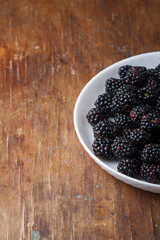 Part of white plate with ripe fresh blackberries visible on wooden old rustic table background. Closeup shot, copy space
