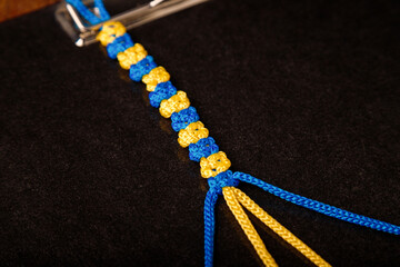 Making process of macrame wristband, paracord bracelet in national Ukrainian flag colors - blue yellow on black background. DIY workshop