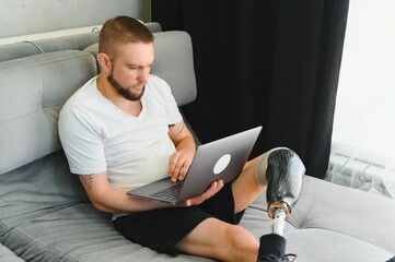 A man with an amputated leg and a prosthetic leg is lying on a bed and working remotely on a laptop