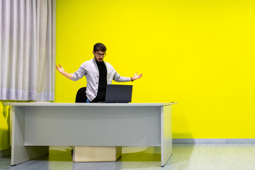 Stressed businessman shrugging at laptop in office with yellow wall