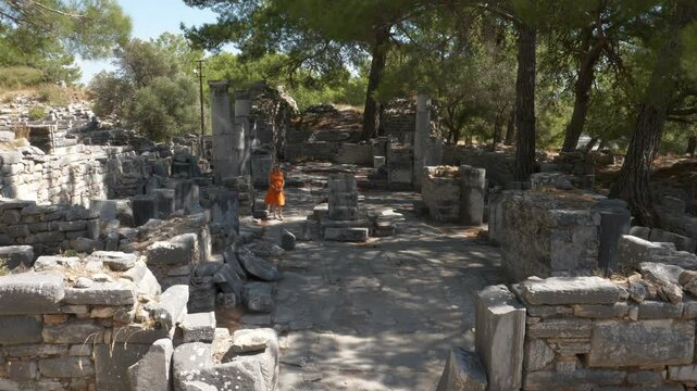 Woman in orange dress walking among historical ruins.