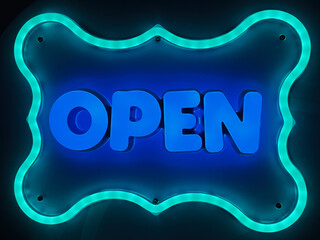 Bright neon sign displaying the text 'Open' with glowing blue lighting