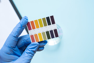 Gloved hand holding ph test strip on light blue surface