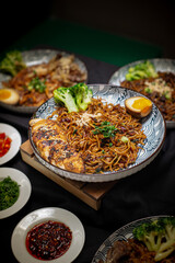 Portrait angle Fried ramen with chili oil served with sliced chicken charsiu and broccoli also with half boiled egg on top. Served on a white and black pattern plate