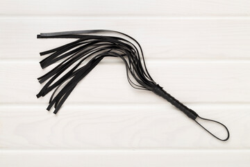 Black whip on wooden background, top view. BDSM concept