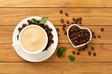 Cup of coffee with coffee beans and leaves on wooden background,top view