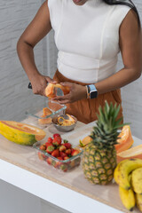 Woman cutting papaya surrounded by fresh tropical fruit on kitchen counter