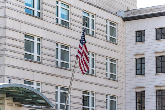 A tall building with a flagpole and an American flag on it. The building is white and has many windows. The flag is flying high and is easily visible from the ground