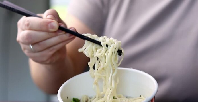 Close up of a female eating simple ramen noodles with chopsticks from a cup
