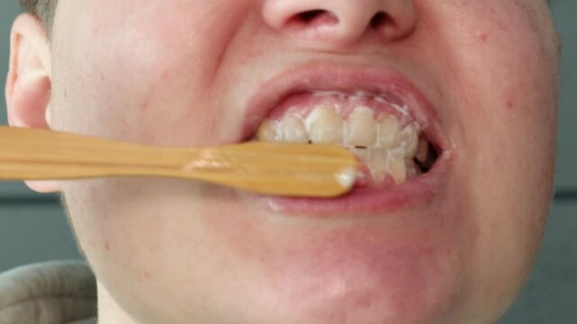 Close-up of person brushing teeth with bamboo toothbrush. Oral hygiene routine using eco-friendly dental care products.
