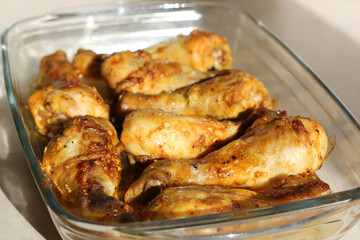 close up of home style crispy roasted chicken legs drumsticks in garlic mayo sauce in a transparent glass cooking dish in kitchen with sunny light background