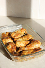 vertical close up of home style crispy roasted chicken legs drumsticks in garlic mayo sauce in a transparent glass cooking dish in kitchen with sunny light background
