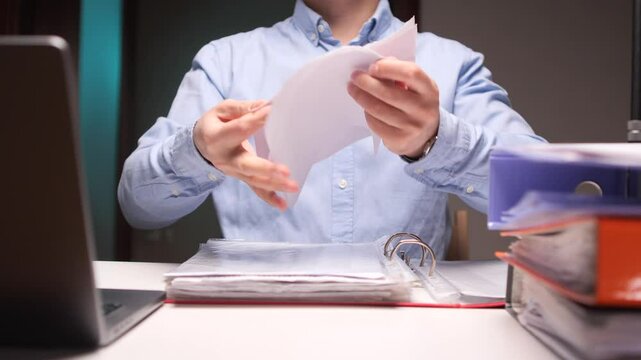Office worker tearing paper document, contract in half at desk with binders and laptop