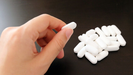 Hand picking up a white supplement tablet from a pile that is placed on a black table.