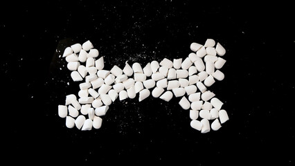 Crushed white supplement tablets arranged in the shape of a bone. With black background.