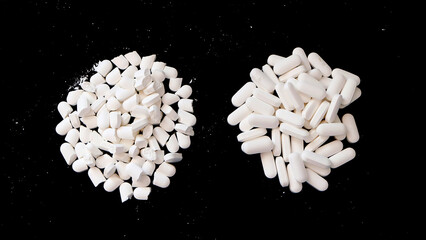 Two piles of white supplement tablets. One pile with whole tablets, and another with tablets split into half. With black background.