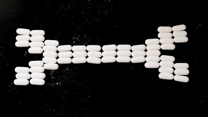 Oval-shaped white supplement tablets arranged in the shape of a bone. With black background.