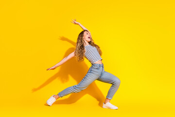 Cheerful young woman striking a dynamic pose against a yellow background, expressing joy, style,...