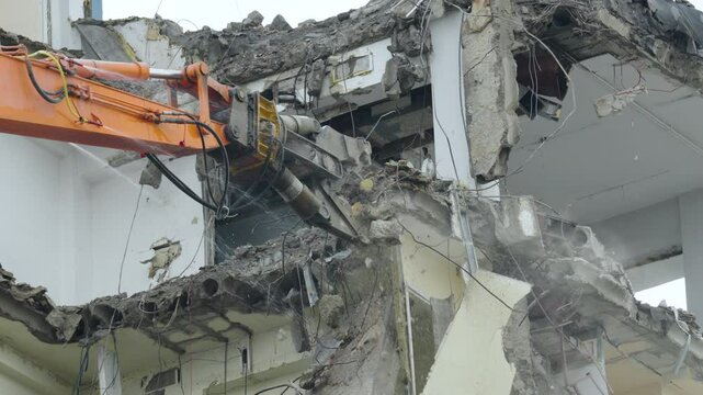 Excavator demolishes damaged building using hydraulic shears in urban area