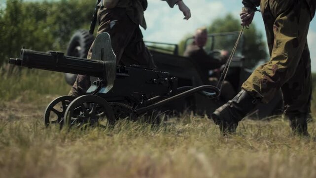 Soviet soldiers transport Maxim machine gun across field. 2 Stormtroopers in historical camouflage uniforms of Red Army pull heavy wheeled machinegun using rope. World War II Reenactment. Battle 1944