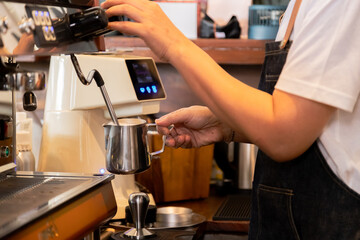 Close-up anonymous barista hands using professional coffee machine making hot espresso and pouring coffee to mug in cozy cafe, small businesses start up for young people lifestyle concept