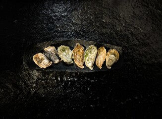 Fresh local oysters are arranged on a slate platter at a bustling fish market. The vibrant display...