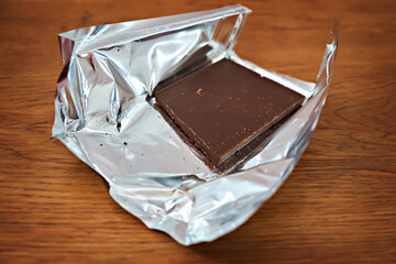 Part of a dark chocolate bar in foil packaging isolated on wooden background. Selective focus