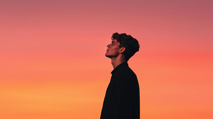 person stands in profile against vibrant sunset sky, creating silhouette effect. warm hues of orange and pink in background evoke sense of calm and introspection