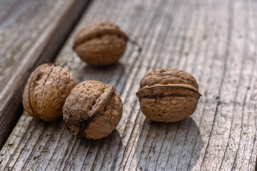 Closeup of four whole walnuts on aged wooden surface with natural textures and warm tones. Organic food, natural patterns, textures, and healthy nutrition. Copy space. Selective focus