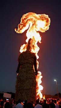 Giant straw effigy burning dramatically at night during festival, fiery traditional event