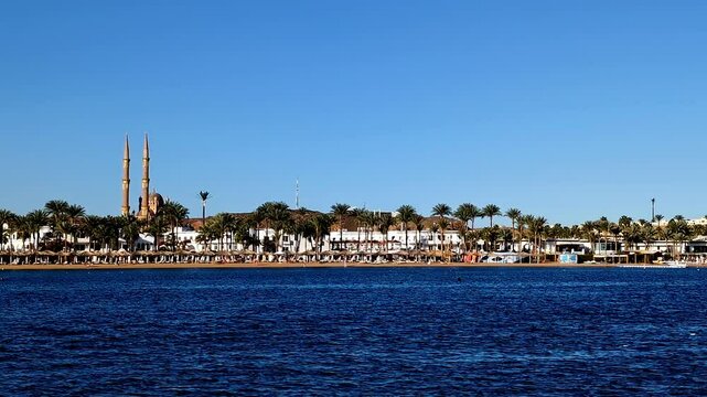 Slow moition shot of coastal scene with row of buildings along the shoreline filled with palm trees in Sharm El-Sheikh, Egypt.