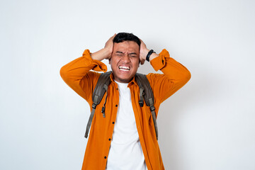 Image of handsome young Asian college student wearing backpack both hands holding head with angry...