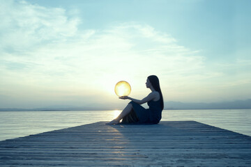 Female figure in backlight holding a moon-shaped lamp in front of a marine sunset