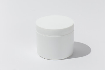 White Cosmetic Cream Jar. Cylinder on textured tan paper with shadows