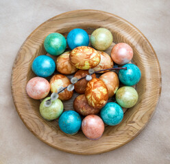 Dyed chicken eggs lay in a round wooden plate with a single sprig of willow on top.
