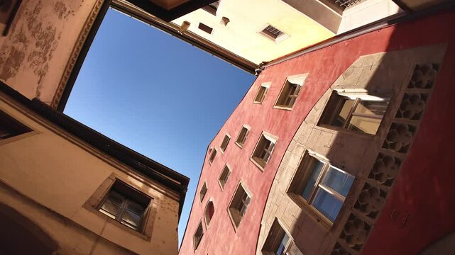 Tiny square or public patio on the street next to the famous old town hall in Regensburg, Germany. Slow motion panning video of looking up between colourful houses or buildings with clear blue sky.