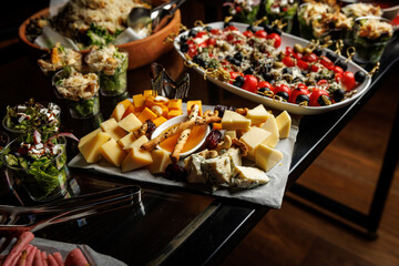 Assorted cheeses and nuts artfully arranged on a platter, accompanied by fresh salads in cups and diverse appetizers. The display is suitable for a gourmet gathering or buffet setting.