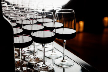 Multiple wine glasses filled with red wine are arranged in a neat row on a reflective surface.