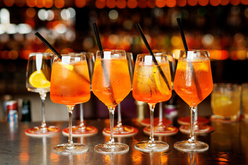 Aperol Spritz cocktails with fresh orange slices in elegant glassware, arranged in a row against a blurred, warm background