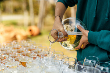 The waiter is pouring white wine from decanter to glasses before the outdoor party