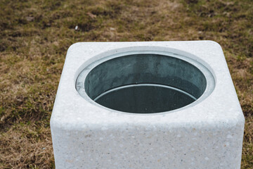 In a lush area of grass, a squareshaped trash can is distinctly placed, making its presence known...