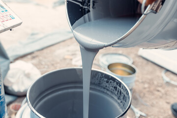 Construction worker pouring gray epoxy coating into bucket for floor finishing