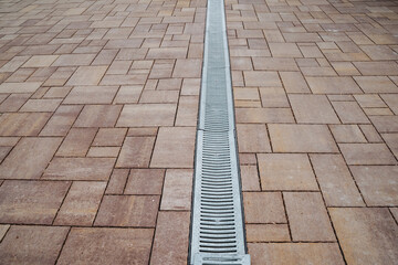 This captivating image provides a closeup of a drain in a brick driveway, highlighting the...