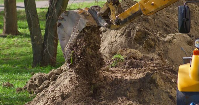Mini Excavator digs a trench for laying a water supply network in the city. A dug hole and a lot of soil around. Close-up Slow motion video in 4k quality.