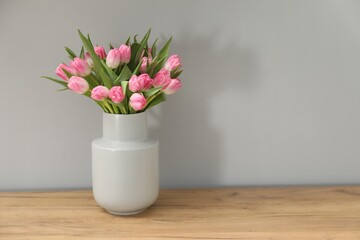 Bouquet of beautiful tulips in vase on wooden table against light grey background, space for text