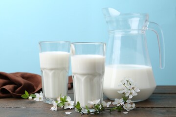 Fresh milk and blossoms on white table against light blue background