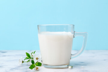 Cup of milk and blossoms on white marble table against light blue background