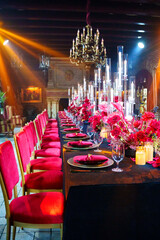 Beautiful festive table setting with fresh red flowers, napkins and candles.