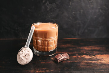 Healthy protein milkshake in a glass, scoop with whey protein powder and chocolate pieces on a dark...