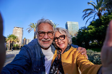 Senior couple taking a cheerful selfie in a park in the city center, enjoying the retired life and...